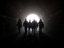 Silhouette Of A Group Of Hikers Walking In A Dark Tunnel
