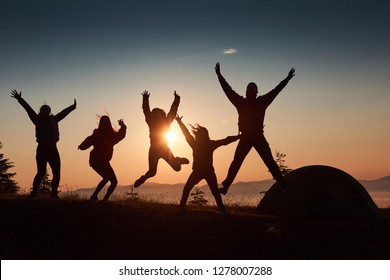 A Silhouette Of Group People Have Fun At The Top Of The Mountain Near The Tent During The Sunset.