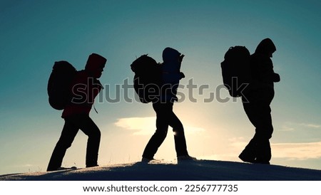 Silhouette of group of tourists, travelers, extending helping hand to each other, climbing snowy slope, mountains. Teamwork, business. Climbers man woman hand in hand. Teamwork business people partner