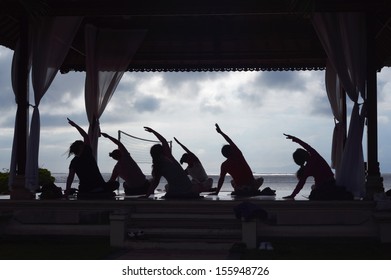 Silhouette Of Group Of Women Practicing Yoga On Beach In Morning