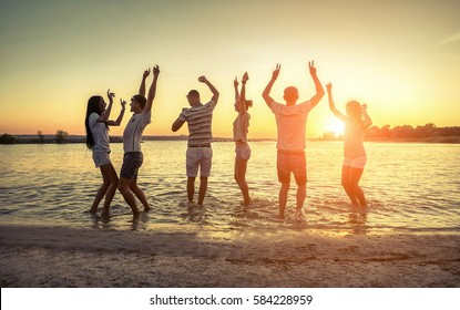 Silhouette of group young people on the beach under sunset sky with clouds at summer evening.