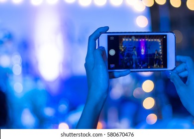 Silhouette of guest hands using smartphone as camera to take pictures and videos of wedding ceremony on stage with bokeh light. Audience taking photo of concert or events by mobile phone at night.