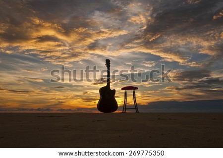 Silhouette Guitar with Chair at The Beach During Sunset Moment Image has grain or blurry or noise and soft focus when view at full resolution.  (Shallow DOF, slight motion blur) 