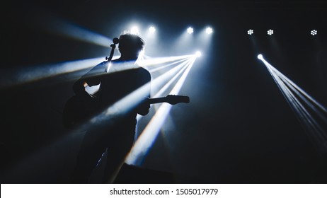 Silhouette Of Guitar Player Performinf On Concert Stage. Dark Background, Smoke, Concert  Spotlights