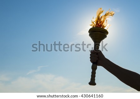 Silhouette of hand of an athlete holding sport torch backlit by bright sun against tropical blue sky