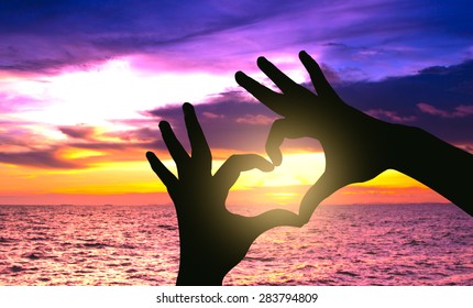 Silhouette hand in heart shape on sunset over the sea
