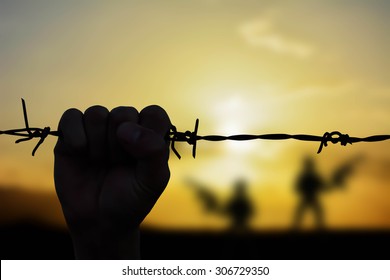 Silhouette Of Hand Holding Barb Wire Fence With Sunset Background