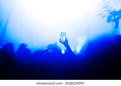 Silhouette of a hand holding a smartphone capturing a moment during a night concert lit by stage lights - Powered by Shutterstock