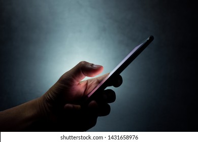 silhouette hand holding and touching a mobile phone screen in the dark darkness against dark blue background  