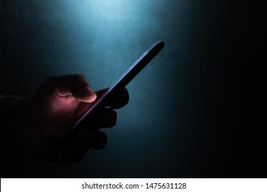 silhouette hand holding and touching a mobile phone screen in the dark darkness against dark blue background  