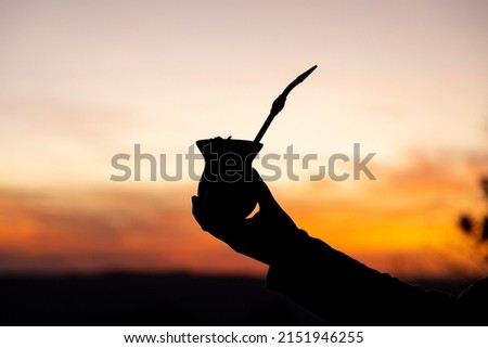 Silhouette of a hand holding a yerba mate gourd drink at sunset. Traditional South American drink. Twilight sky