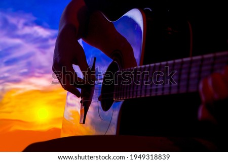 silhouette hand of musician playing acoustic guitar at sunset