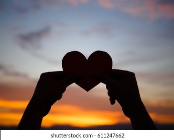 silhouette hand is raising the red paper heart with blur sunlight during sunset, Valentines day