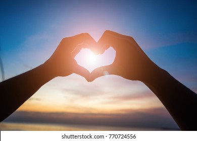 Silhouette Of Hand Sign Heart On Twilight Sky After Sunset. Subject Is Blurred And Low Key.