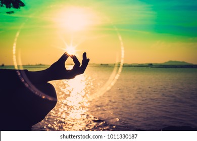 Silhouette, A Hand Of Woman Meditating In A Yoga Pose Or Lotus Position At The Sea In Sunset And Reflection Of Sunlight. Nature Meditation And Spa Like Zen Or Calm And Solitude Concept. Relax Time.