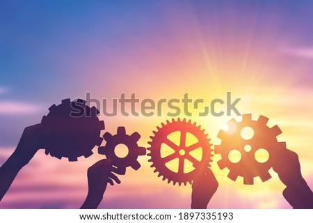 Silhouette hands holding gear from at sunlight background. concept of a teamwork cooperation idea.
