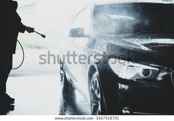 Silhouette of hands of a man washing black car\
outdoors in a carwash station, using water jet with high pressured\
water stream