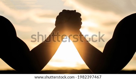 Silhouette of hands that compete in strength. Rivalry, closeup of male arm wrestling. Men measuring forces, arms. Two men arm wrestling. Rivalry, vs, challenge, strength comparison. Sunset, sunrise.