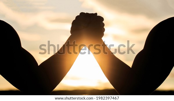 Silhouette of hands that compete in strength.\
Rivalry, closeup of male arm wrestling. Men measuring forces, arms.\
Two men arm wrestling. Rivalry, vs, challenge, strength comparison.\
Sunset, sunrise.