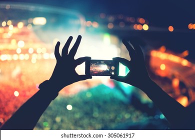 Silhouette Of Hands Using Camera Phone To Take Pictures And Videos At Pop Concert, Festival. Soft Effect On Photo