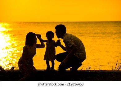 Silhouette Of Happy Asian Family Playing At Outdoor Beach During Summer Sunset.