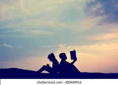 Silhouette of happy boy and girl reading a book in the sky sunset ,free time on holiday - Powered by Shutterstock