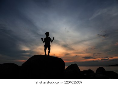 Silhouette happy boy playing on top of rock with dramatic sky at tropical sunset. - Shutterstock ID 1204015339