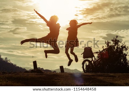 Silhouette of happy children jumping playing on mountain meadow at sunset time