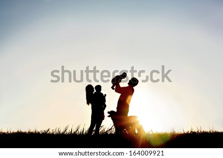 A silhouette of a happy family of four people, mother, father, baby, and child, and their dog in front of a sunsetting sky, with room four copy space or text
