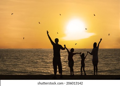 Silhouette Of Happy Family On Beach Watching Sunset Together