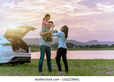 Silhouette the happy family of three people, mother, father and child in front of a sunset sky; asian family are happy sitting in the open trunk of a car; travel nature trip.