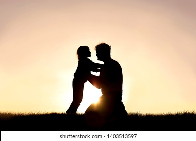 A silhouette of a happy father and his little child are smiling and embracing as they play outside at sunset at the end of a summer day.