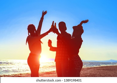 Silhouette Of Happy Friends Dance At Beach Party On Sunrise  Light - Teenagers Cheers With Beer Bottles Having Fun  Moment On Summer Holiday - Concept Of Teenage Friendship - Soft Bluish Filter Image