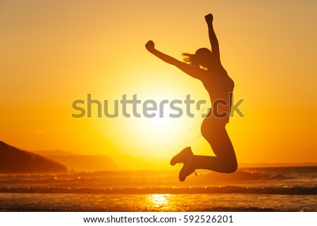 Silhouette of happy joyful woman jumping and having fun at the beach against the sunset. Freedom and leisure vacation concept.
