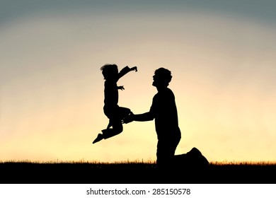 A silhouette of a happy little boy child is jumping into the loving arms of his father isolated against the sunset on a summer day.