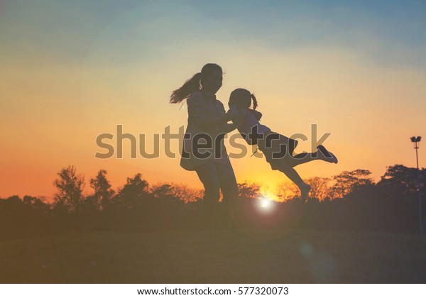 太陽の光に照らされて抱きしめる愛する母親の腕に駆け込む幸せな少女の子どものシルエット 日没の前 タイ バンコク市のチャトチャク公園にある空に浮かぶ 友好的な家族のコンセプト の写真素材 今すぐ編集