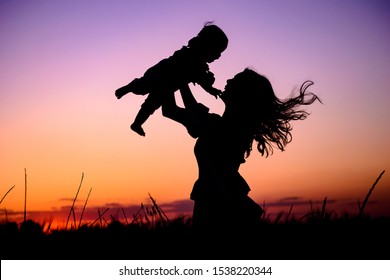 Silhouette happy mother and baby. Mother plays with her baby in her arms under the rays of the sunset in a meadow. Motherhood concept. Happiness, inspiring, joyful moments. Mother's day concept. - Shutterstock ID 1538220344