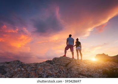 Silhouette of happy people on the mountain against colorful sky at sunset. Landscape with silhouettes of a standing man and woman with holding hands on the mountain peak in summer. Traveling couple
