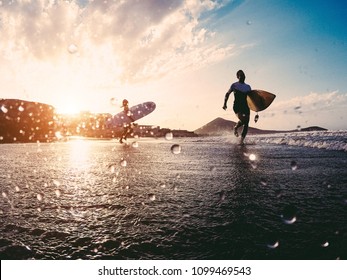 Silhouette of happy surfers running with surf boards on the beach - Sporty people having fun in sunny day - Extreme sport, travel and vacation concept - Focus on right male body - Powered by Shutterstock