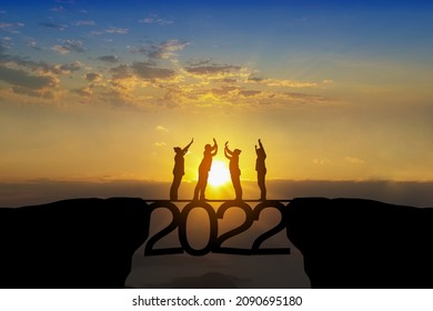 Silhouette of happy teamwork standing at the top of 2022 text on beautiful sunrise background celebrate business success ,goal achievement and growth to year 2022.