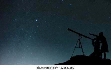 Silhouette happy time of boy and girl with telescope on the rock at the star background 