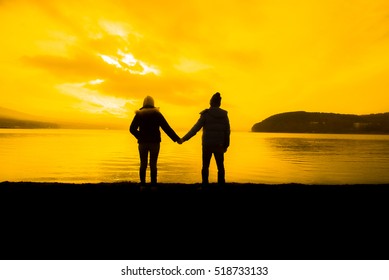 Silhouette of Happy Young Couple Hugging Outside at Sunset
