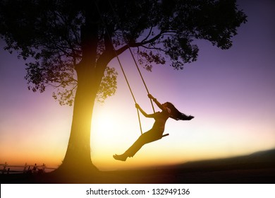 silhouette of happy young woman on a swing with sunset background - Powered by Shutterstock