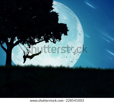 Silhouette of happy young woman on a swing of a tree isolated on beautiful background of moon, earth, night skyline, falling stars. Body vitality, human spirit well being, freedom, happiness concept