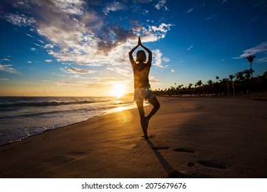 Silhouette healthy woman doing Yoga exercises on the beach in sunset time. Female meditation at sunrise seaside