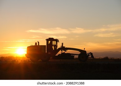 Silhouette Of Heavy Duty Tractor Driving On Road At Sunset