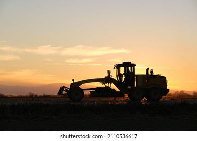 Silhouette Of Heavy Duty Tractor Driving On Road At Sunset