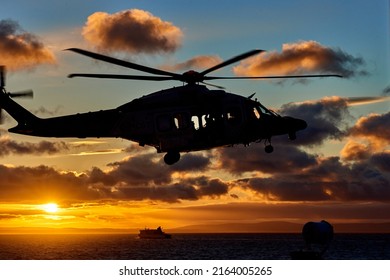 Silhouette Of Helicopter Of Coast Guard Approaching To Vessel For Training Exercise On Sunset Background