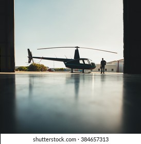 Silhouette Of Helicopter With A Pilot Walking In The Airplane Hangar After The Flight.