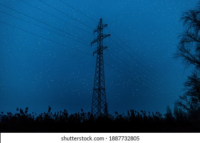 Silhouette Of High Voltage Electric Power Transmission Lines Tower, In The Middle Of A Field Against A Blue Night Sky With Stars